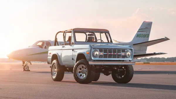 Restored classic Ford Bronco in front of a private plane